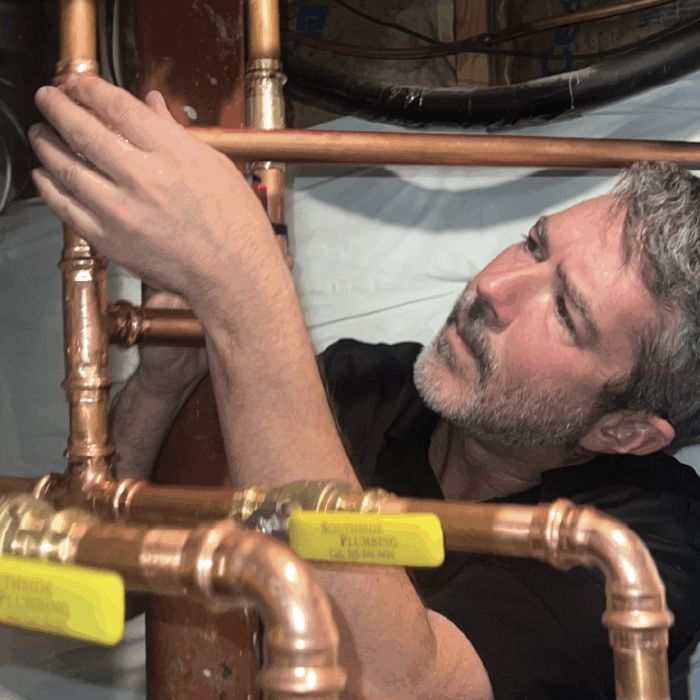 Plumber examining piping going into water heater.